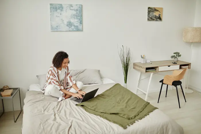 Une étudiante, assise sur le lit de son logement étudiant, en train de réaliser les démarches en ligne pour obtenir une aide au logement alternance