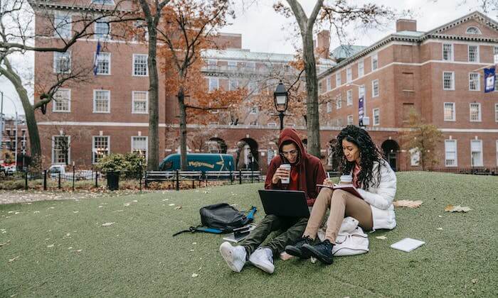 Un jeune homme et une jeune femme assis sur un campus, regardant un ordinateur portable et buvant des jus dans des gobelets