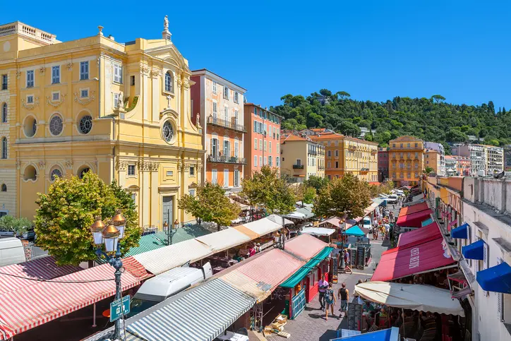 Vue sur un quartier de Nice, on voit les bâtiments colorés et la rue marchande en un jour ensoleillé. L'appartement étudiant à Nice est disponible dans ce type de quartier animé.