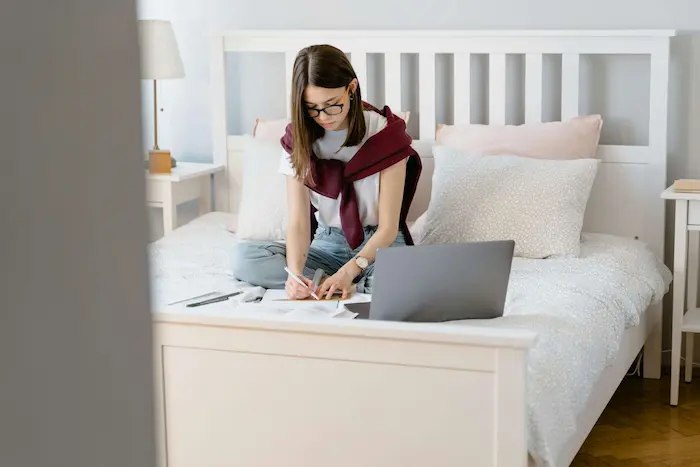 Une étudiante qui est en train d'étudier dans sa chambre en résidence universitaire à Aix-en-Provence. On y voit un lit et un PC.