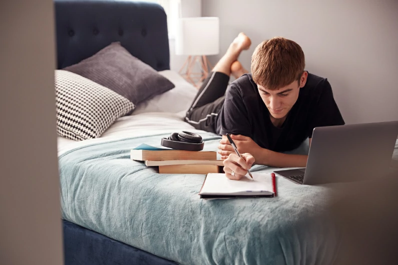 résidence étudiante à Cergy : dans son appartement, sur son lit, cet étudiant revoit ses prises de notes durant les cours et révise. Etude en résidence.