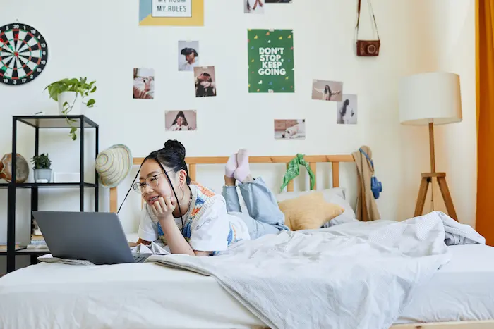 Une étudiante travaille sur son ordinateur sur un lit, dans une chambre chez l'habitant à Tours