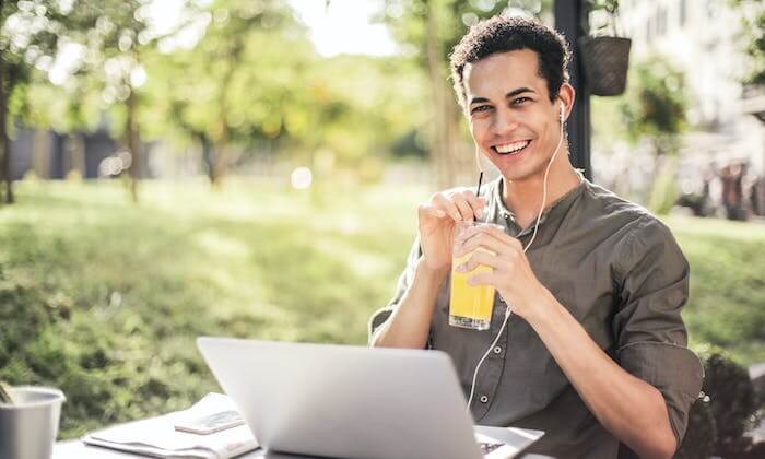 Un homme assis sur le campus en train d'étudier sur son ordinateur portable tout en souriant