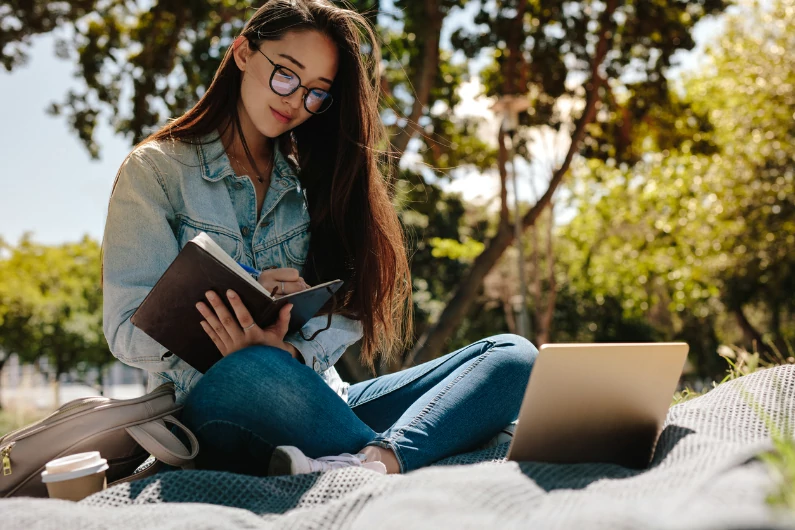 résidence étudiante à Clermont-Ferrand : une étudiante est assise dans la cours du campus en solitaire pour profiter du bon temps et étudier. Vie universitaire.