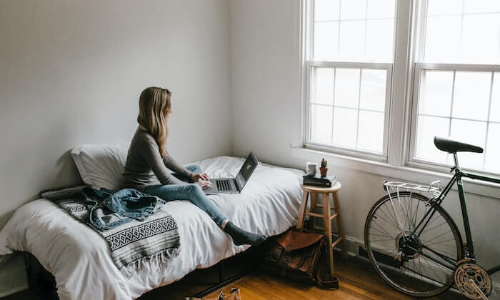 Étudiant assis sur son lit avec son ordinateur, étudiant dans un environnement confortable et propice à l'étude