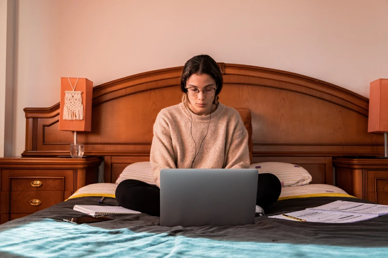 résidence étudiante à Clamart : une étudiante travaille en ligne depuis son ordinateur sur son lit. Job étudiant et vie universitaire.