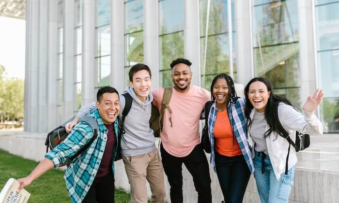 Un groupe de cinq étudiants souriants prenant une photo devant l'école